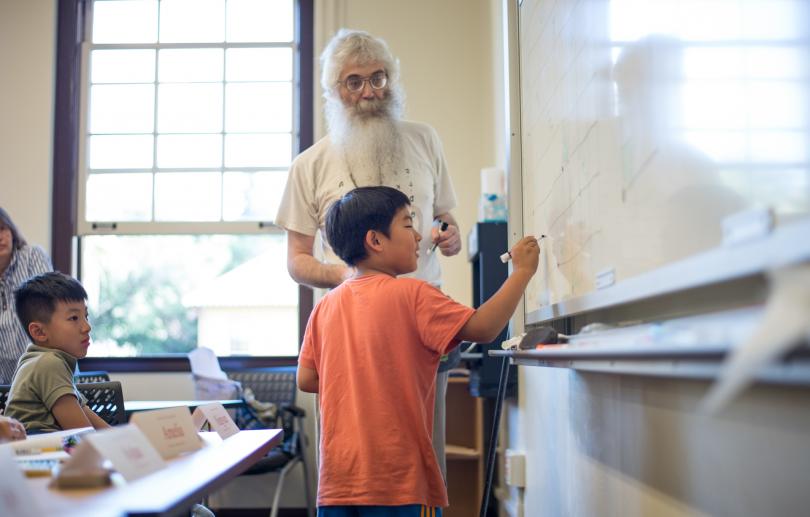 An instructor works with a young student at the whiteboard during a Stanford Math Circle session.